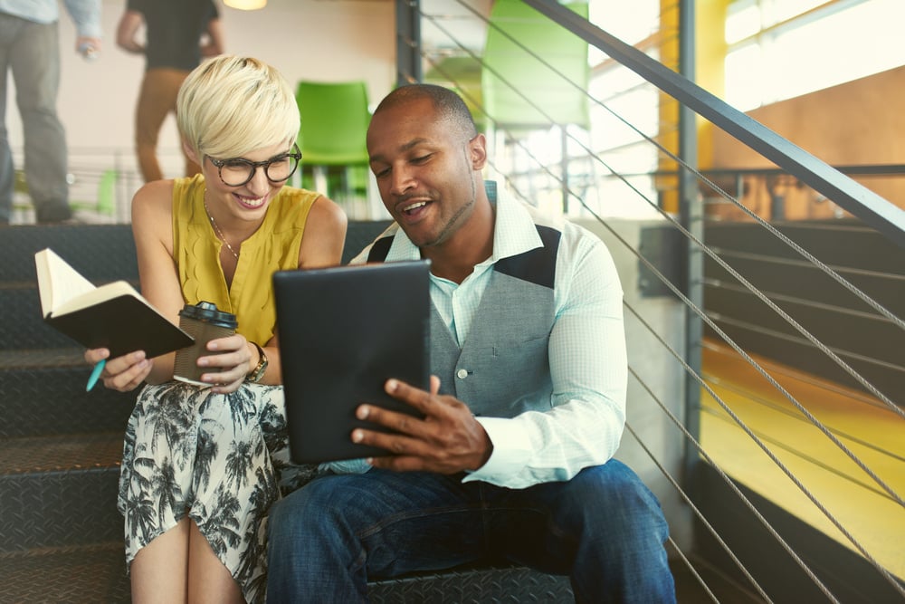Two creative millennial professionals using a digital tablet while sitting on staircase